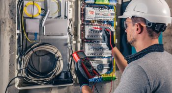 Man, an electrical technician working in a switchboard with fuses. Installation and connection of electrical equipment. Professional uses a tablet.